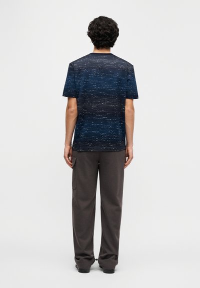 Short-sleeve, navy blue t-shirt with a textured pattern, paired with grey loose-fitting pants, viewed from the back.