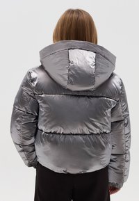 Silberne Pufferjacke mit glanzvollem, gesteppte Textur und einer großen Kapuze. Verfügt über horizontale Nähte und elastische Bündchen für Wärme.