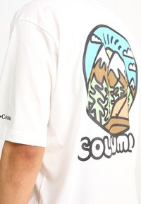 Camiseta blanca de algodón con un gráfico colorido de montañas, árboles y una tienda en la parte posterior, con "Columbia" impreso en la manga.