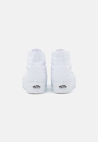 Hvide høje sneakers med quiltet detaljer og en flad platformssål med et sort Vans-logo på hælen. Glat canvasmateriale.