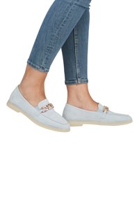 Helle blaue Wildleder-Leder loafers mit einer Kettenakzent, flacher beiger Sohle und einem minimalistischen Design; kombiniert mit geschnittenen Denim-Jeans.