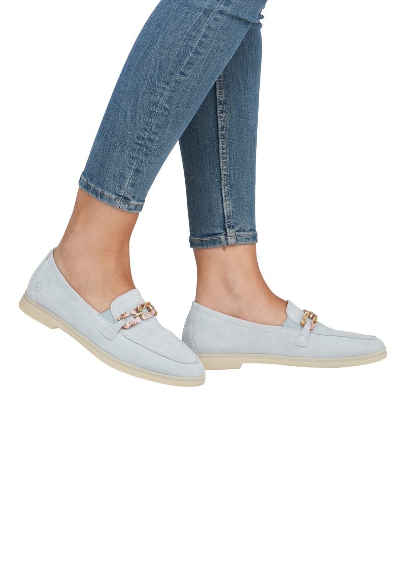 Helle blaue Wildleder-Leder loafers mit einer Kettenakzent, flacher beiger Sohle und einem minimalistischen Design; kombiniert mit geschnittenen Denim-Jeans.