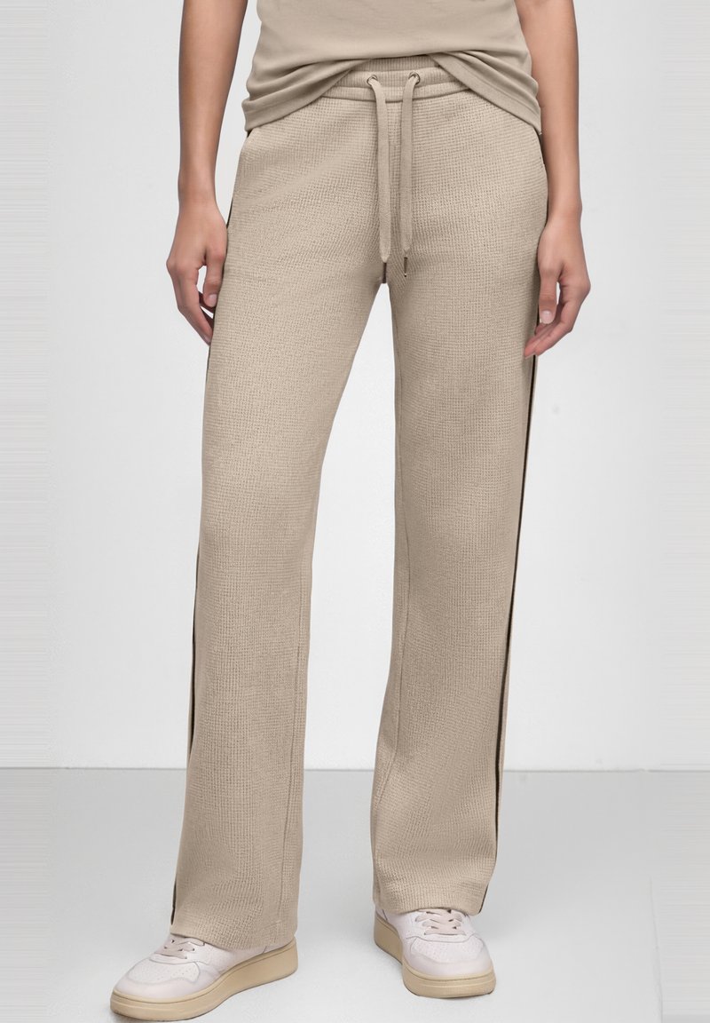 Pantalones anchos texturizados color beige con cintura de cordón, combinados con zapatillas beige y top a juego, mostrados desde la mitad del torso hasta los pies.