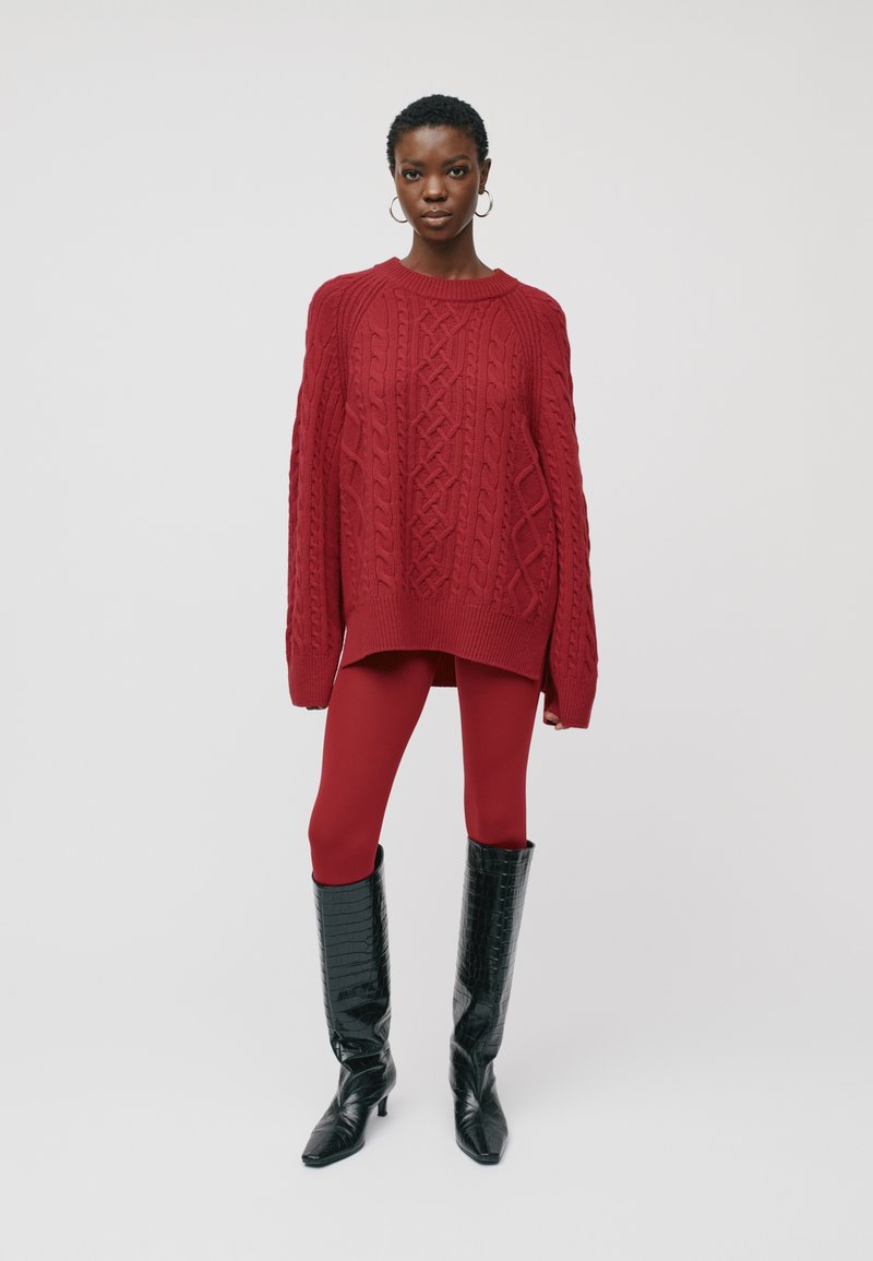 Raudonas megztinis su kabeliu, didelio dydžio, derinamas su raudonomis kelnėmis ir blizgiomis juodomis aukštakulnėmis batais iki kelių, su smailėmis.