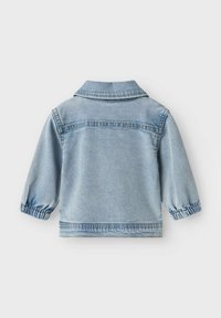 Světle modrá džínová bunda, pohled zezadu. Má klasický límec, elastické manžety a viditelné detaily šití. Hladká textura.