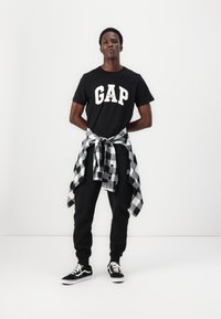 Black GAP t-shirt with white lettering, black sweatpants, tied black and white checkered flannel around the waist, black sneakers.