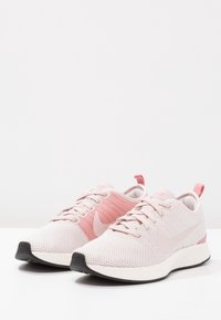 Ljusrosa sportskor med ovandel i mesh, kontrasterande rosa detaljer, rund tå, snörning och svart sula. Slät yta.