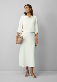 Witte top met kraag en midi-rok duo met een gladde textuur. De combinatie heeft een lichtbeige gestructureerde handtas en sandalen met kruisbanden.