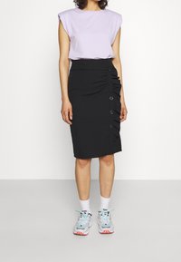 Fialový top s krátkým rukávem v kombinaci s černou pouzdrovou sukní s bočním nařasením a knoflíky. Model má na sobě tenisky s modrými akcenty a bílé ponožky.