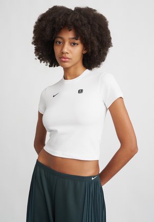 White cropped t-shirt with short sleeves, featuring a black Nike logo on the chest and a small branded detail. Smooth fabric texture.