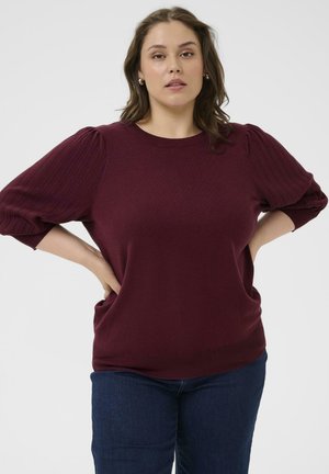 Burgundy knit top with ribbed puff sleeves, round neckline, and relaxed fit. Paired with dark blue denim jeans.