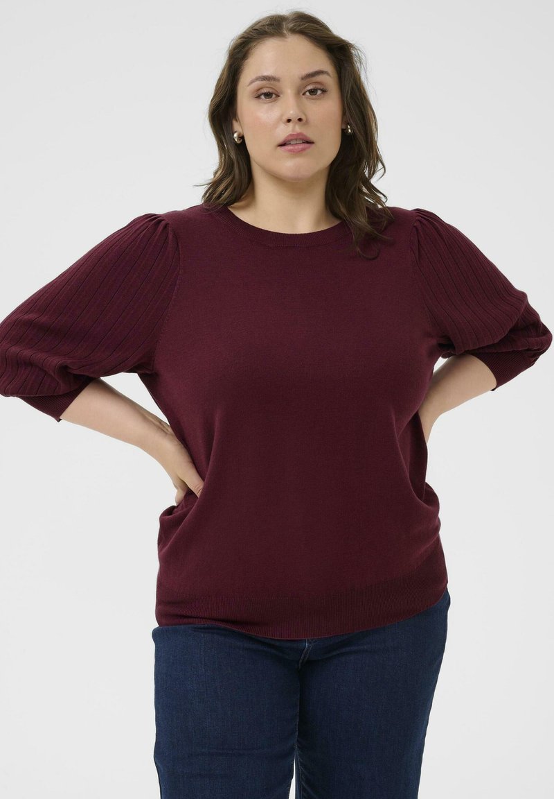Top en tricot bourgogne avec des manches bouffantes côtelées, un col rond et une coupe décontractée. Associé à un jean en denim bleu foncé.