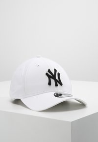 Valkoinen baseball-lippis, joka on valmistettu kankaasta ja jossa on kohotettu musta "NY"-logo. Kaareva lippa ja säädettävä hihna takana, sileä pinta.