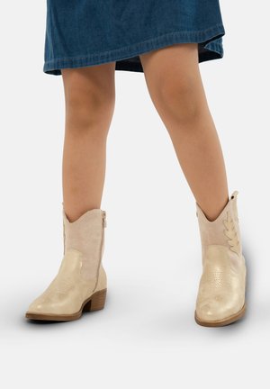 Beżowe botki do kostki o teksturowanej powierzchni, z dekoracyjnym przeszyciem i tłoczonym wzorem liści. Obcas jest niski i drewniany.