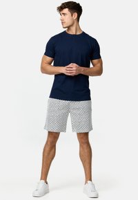 T-shirt bleu marine à manches courtes avec col rond et détail de bouton, associé à un short blanc avec un motif en zigzag noir. Baskets blanches.