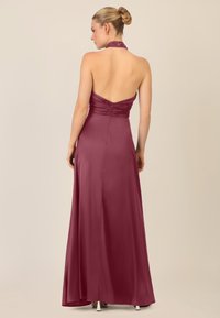 Langes, ärmelloses Abendkleid in Burgunderrot mit Halterneck und gerafft gearbeitetem Oberteil. Glatte, seidig-texturierte Fabric und Reißverschluss auf der Rückseite.