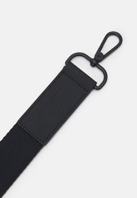 Zwarte stoffen band met een rechthoekige rubberen patch met reliëfbranding en een zwarte metalen clip voor bevestiging.