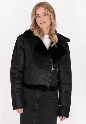 Veste en simili cuir noire avec un col en fourrure, fermeture éclair asymétrique et finition texturée. Style ajusté avec des manches larges.