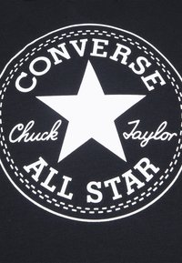 Zwarte stof heeft een grote witte cirkelvormige grafiek met een ster in het midden. De tekst bevat "CONVERSE," "Chuck," en "Taylor" in verschillende lettertypes.