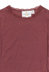 Top rigato color bordeaux con una consistenza morbida, caratterizzato da un collo a scallop e due bottoni a pressione sulla spalla. Etichetta visibile con il nome del marchio.