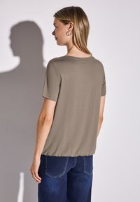 Top de corte relajado y manga corta en tela verde oliva; escote redondeado; textura suave; combinado con jeans azul oscuro; diseño sencillo.