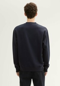 Felpa blu navy con collo a giro, maniche lunghe e polsini a coste. Tessuto morbido con una texture liscia, design semplice senza motivi.