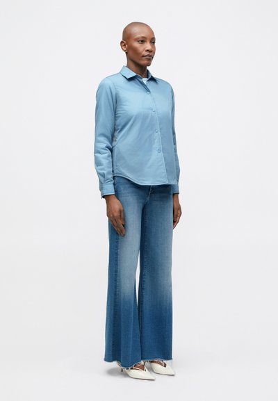 Lichtblauw overhemd met lange mouwen, gedragen met wijde, vervaagde denim jeans en witte puntige hakken. Strakke lijnen en casual pasvorm.