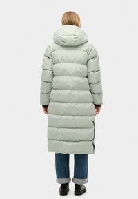 Lang, lys grøn dunjakke med vandret syninger, hætte og sidespalter, parret med optrillede jeans og sorte ankelstøvler.