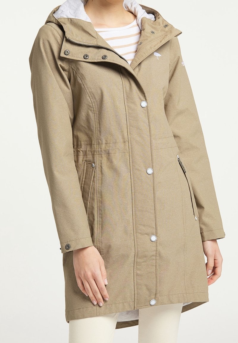 Veste imperméable beige avec capuche, fermeture avant par boutons-pression et zip, poches latérales, et tissu texturé. Doublure intérieure contrastante grise.