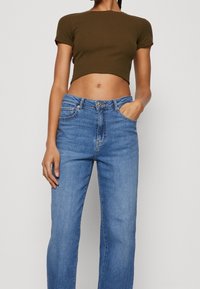 Olivgrön ribbad crop-top som matchas med ljusblå högmidjade raka jeans, som har klassisk femfickdesign och metalldetaljer.
