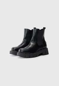Zwarte leren enkelboots met elastische zijkanten, chunky zwarte rubberen zolen en stikseldetails langs de randen voor extra textuur.
