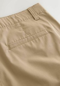 Gros plan sur un pantalon beige montrant la poche arrière et la boucle de ceinture avec des coutures visibles et une texture de tissu lisse.