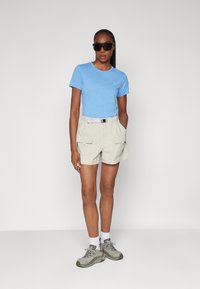 Lys blå t-shirt, beige cargo shorts med lommer og grå sneakers. Sorte solbriller fuldender outfittet. Simpelt og funktionelt design.