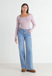 Lys lilla langermet tettsittende topp med knapper, kombinert med høy midje, vide lys blå jeans og brune sko. Enkle, glatte teksturer.