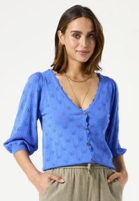 Cardigan bleu texturé avec un col en forme d'ondulation et des manches trois-quarts. Caractérisé par des boutons décoratifs et un motif subtil ressemblant à des feuilles.