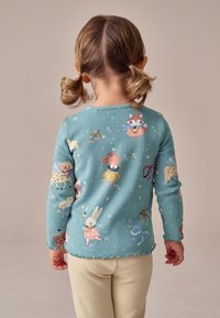 Hosszú ujjú, bordázott türkiz felső játékos állatillusztrációkkal és csillagokkal, hullámos szegéllyel és testhezálló kialakítással.