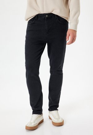 Jean en denim noir avec une coupe slim, cinq poches et une fermeture à bouton. Associé à des baskets blanches avec des accents beiges.