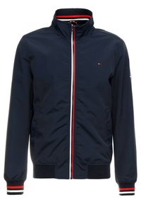 Námořnická modrá bunda na zip s vysokým límcem, červenými a bílými pruhy na límci, zipu a manžetách, a malým logem na hrudi a rukávu.