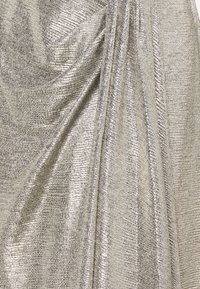 Metallic silver fabric with a textured, woven pattern, draped to create soft folds and movement. Reflective surface adds depth and interest.