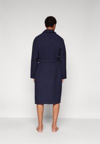 Navy blue bathrobe with long sleeves, textured fabric, belted waist, and knee-length cut, viewed from the back.