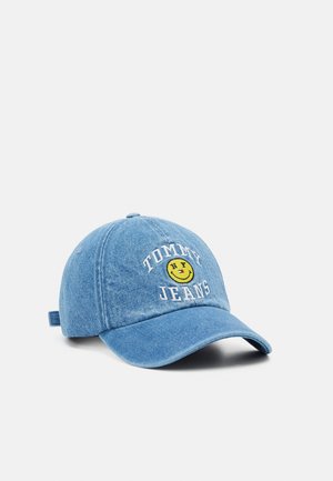 Lichtblauwe denim baseballpet met geborduurde tekst "Tommy Jeans" en een gele smiley met één knipperend oog en uitgestoken tong.