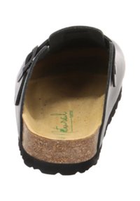 Black open-back shoe featuring a smooth exterior, cork footbed, and textured rubber sole, with a small decorative bow accent.