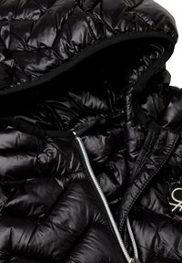 Černá prošívaná bunda s kapucí, se zipovým uzávěrem a kontrastní černou podšívkou. Přítomný výrazný detail loga.