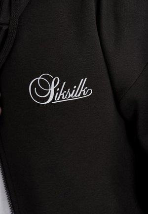 Čierna mikina na zips s textúrovanou tkaninou, s výrazným bielym vyšitým logom "SikSilk" na ľavej strane hrudníka.