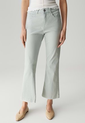 Lichtgroene uitlopende jeans met een zachte textuur, vijf-pocket ontwerp, sluiting met een voorknoop en subtiele stikdetails. Gecombineerd met beige schoenen.