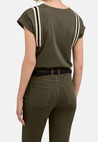 Olivově zelené tričko s ohrnutými rukávy a černobílými pruhy na ramenou; nošeno s odpovídajícími olivově zelenými kalhotami a černým opaskem.