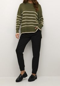 Maglione a righe verde oliva con bande color crema, vestibilità oversize, polsini a coste. Pantaloni neri a gamba affusolata, con vita elasticizzata, abbinati a mocassini neri chunky.