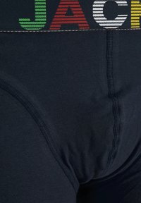 Los calzoncillos de hombre en azul oscuro presentan una cinturilla contrastante con letras rayadas en verde, rojo, blanco y amarillo. Tienen una textura suave y una forma ajustada.