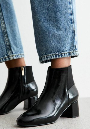 Zwarte gepatineerde leren enkellaarsjes met een blokhak, voorzien van elastische zijkanten en een rits aan de zijkant. Gemaakt in combinatie met lichtblauwe cropped spijkerbroek.