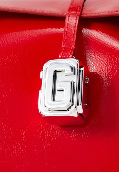 Punainen kiiltävä keinonahkakäsilaukku, jossa on kiiltävä hopeatonssi ja "G"-logo. Sujuva pinta ja jämäkkä muotoilu.